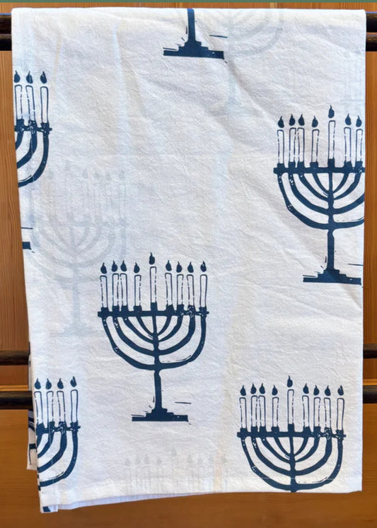 The Rustic County Festival of Lights Tea Towel features a white cloth with blue menorah patterns and nine lit candles, making it the perfect Hanukkah kitchen towel and festive holiday decor.