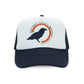 A Rustic County trucker hat with a navy blue brim and mesh backing, featuring a white front panel with an orange and blue logo that includes a silhouette of a crow and the text "Rustic County".