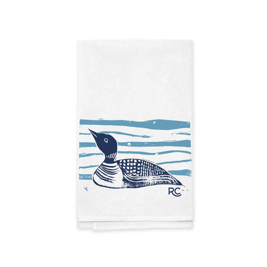 A Rustic County Maine Loon Kitchen Tea Towel featuring a blue print of a Maine loon on water, with stylized waves and the initials "rc" in the corner.