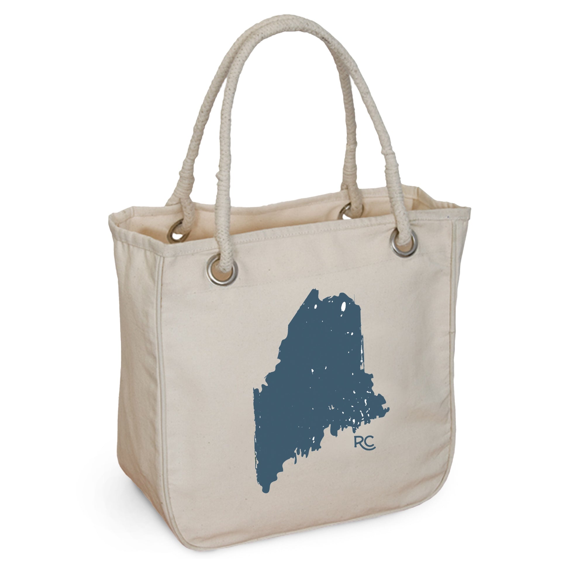 The Maine Rope Tote from Rustic County is made of organic cotton, featuring beige canvas, rope handles, and a blue state silhouette with "RC" initials. It embodies eco-friendly style for daily use.