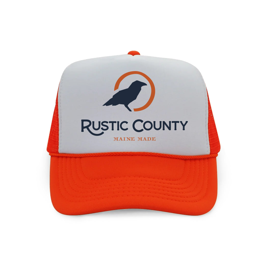 A white and blaze orange Rustic County Trucker Hat with the "Rustic County Maine Made" logo featuring a silhouette of a bird on the front panel, isolated on a white background.