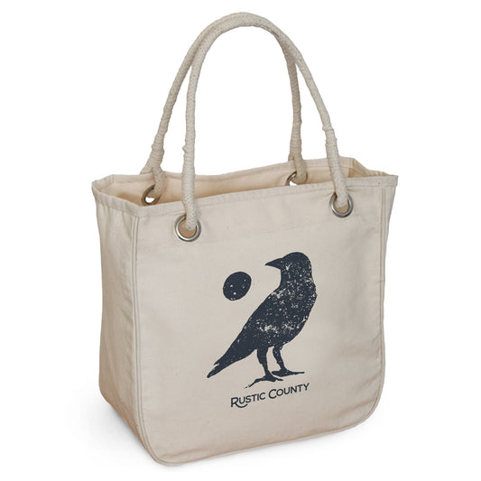 A beige Full Moon Crow Rope Tote bag with rope handles, featuring a black print of a crow holding a full moon. The words "Rustic County" are printed above the image.