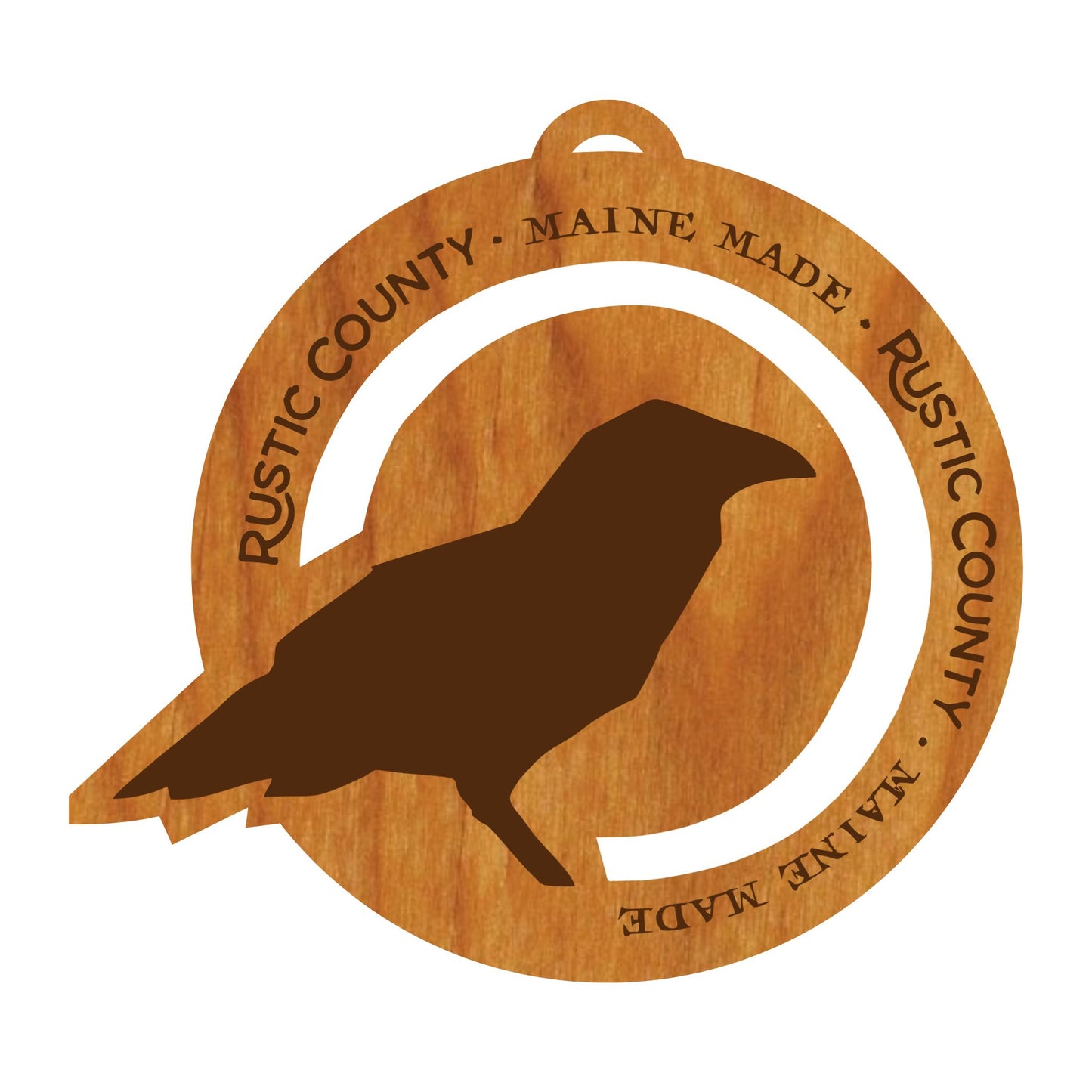 A wooden coaster with a burnt-in design of a crow silhouette, encircled by text that reads "Rustic County Maine made. Rustic made." designed to appear like a vintage label, the Rustic County Ornament.
